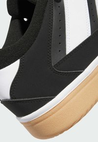 Svart och vit sneaker med en texturerad ovandel, vadderad krage och en sula av gummigummi. Stickad detaljering och perforeringar syns.