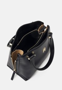 Sac à main en cuir noir avec fermeture éclair dorée et logo, ouverture supérieure montrant plusieurs compartiments et doubles poignées sur fond blanc.