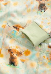 Langærmet tøj lavet af blødt stof, med et pastelfarvet blomsterdesign der inkluderer tegneserie Highland-køer. Grønne manchetter tilføjer kontrast.
