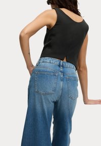 Top aderente nero con scollatura a goccia, abbinato a jeans in denim a gamba larga di un blu chiaro, dotati di due tasche posteriori e una finitura sbiadita.