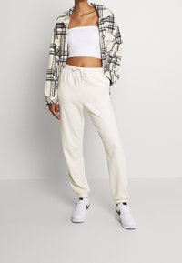 Rutig fleecejacka i krämfärg och svart, vit kort topp och krämfärgade joggare med elastiska mudd, kombinerat med vita sneakers.