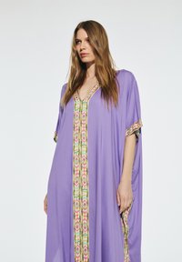 Lila kaftan tillverkad av lättviktsmaterial, med en färgglad mönstrad trim nedtill och detaljer på ärmarna.