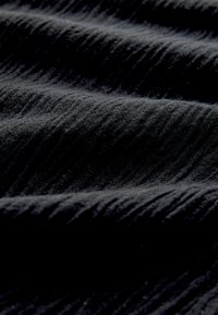 Krupan plan crnog rebrastog tkanja koji prikazuje mekanu teksturu i paralelne uzdignute grebene u nježnim naborema.