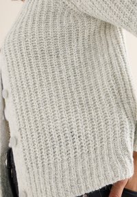 Strickjacke in Hellgrau mit gerippter Textur. Verfügt über runde Knöpfe an der Seite und eine boxy Silhouette.