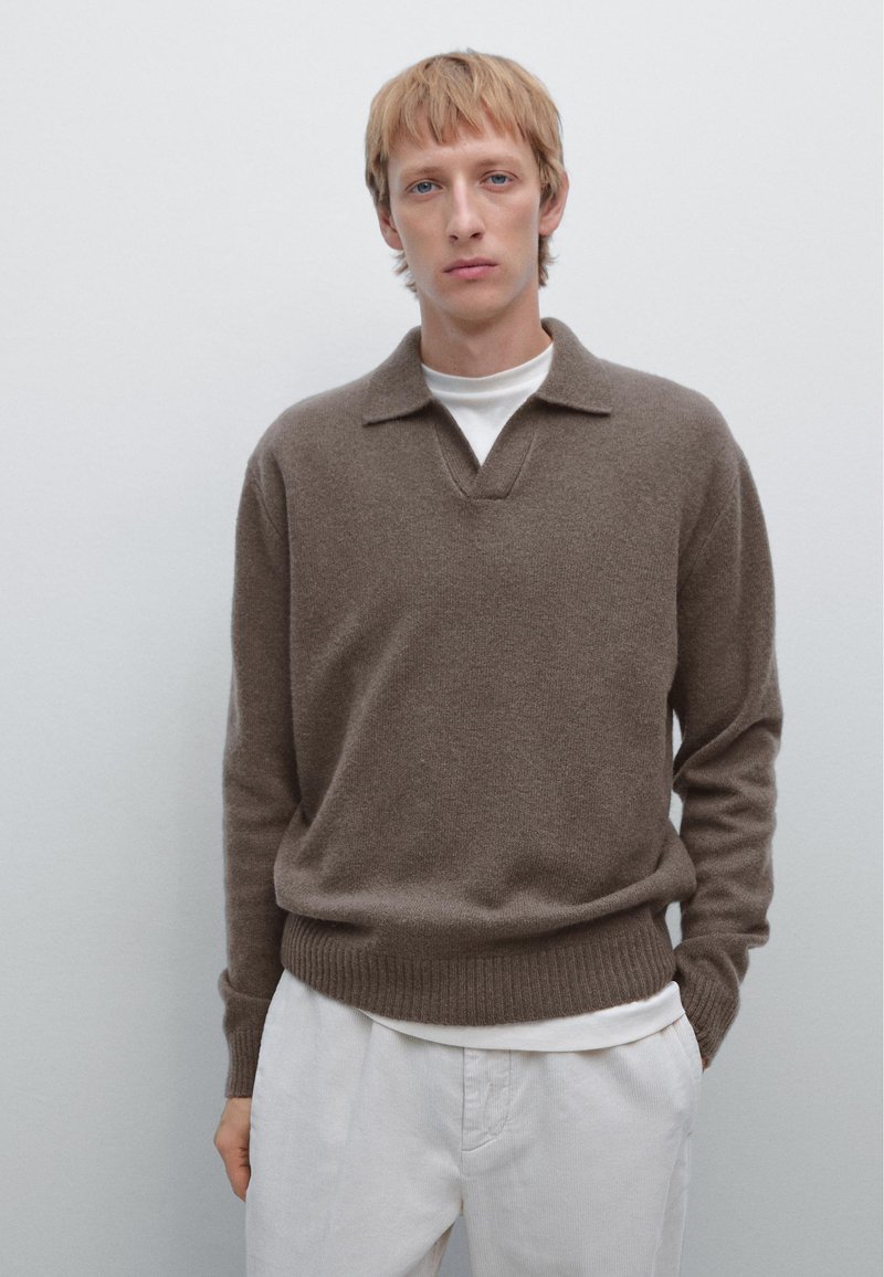 Brown wool sweater with a v-neck and polo collar. Features long sleeves and a ribbed hem. Worn over a white crewneck shirt and light pants.