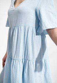 Himmelblaues, gestuftes Kleid aus strukturiertem, leichtem Stoff. Es hat einen V-Ausschnitt und kurze, fließende Ärmel.