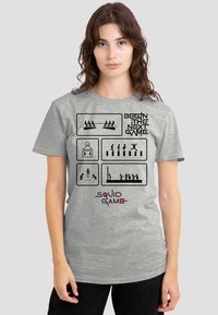 Gray cotton t-shirt featuring black graphic illustrations and text "BEGIN THE NEXT GAME" and "SQUID GAME" in pink, short sleeves, relaxed fit.