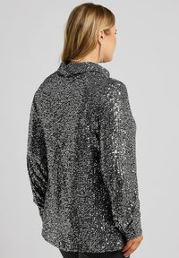 Camicia nera con paillettes, colletto, maniche lunghe e vestibilità rilassata. Presenta paillettes lucide e densamente raccolte, che conferiscono un aspetto testurizzato.