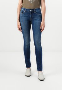 Tynne blå denimjeans med middels høy midje, med et klassisk fem-lommers design og minimal falming. Sammen med lysfargede sko.