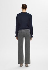 Temno modra majica z dolgimi rokavi, sproščen kroj; kombinirana z visokim pasom, sivimi kavbojkami z ravnimi hlačnicami. Preprost dizajn, z minimalnimi detajli.