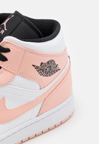Wysokie trampki z różowej i białej skóry, czarnym wyściełanym kołnierzem, czarnymi sznurówkami i logo Air Jordan z skrzydłami po boku.