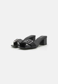 Sandales à talons noirs avec une finition brillante, dotées d'une large sangle avec une boucle métallique carrée et d'une semelle intérieure texturée pour plus de confort.