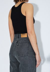 Top tank nero a costine abbinato a jeans scuri a vita alta, con etichetta visibile, design a cinque tasche e una leggera texture scolorita.