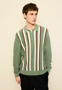 Groen gestreepte polo trui met een ritskraag, voorzien van verticale lijnen in crème en bruin. Ribbelige textuur en lange mouwen.