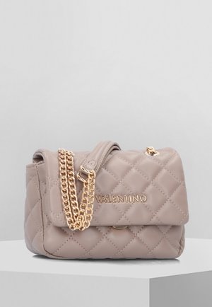Beige gewatteerde Valentino-handtas met een gouden kettingband en logo, rustend op een wit voetstuk tegen een effen achtergrond.