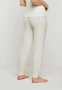 Helle graue, weiche Strickhose mit schmal zulaufenden Beinen und gerippten Bündchen. Verfügt über Seitentaschen und einen lässigen Schnitt. Getragen mit baren Füßen.