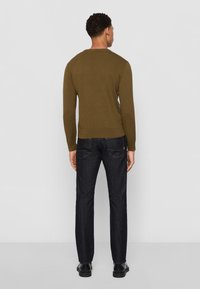 Maglione verde con collo rotondo, abbinato a jeans blu scuro. La trama a maglia è visibile e i jeans presentano un design classico a cinque tasche.