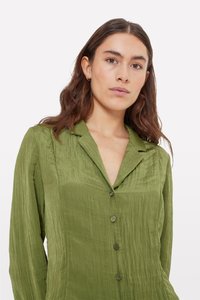 Olive green button-up shirt with a textured, crinkled fabric. Features a notched collar and seven small, dark buttons down the front.