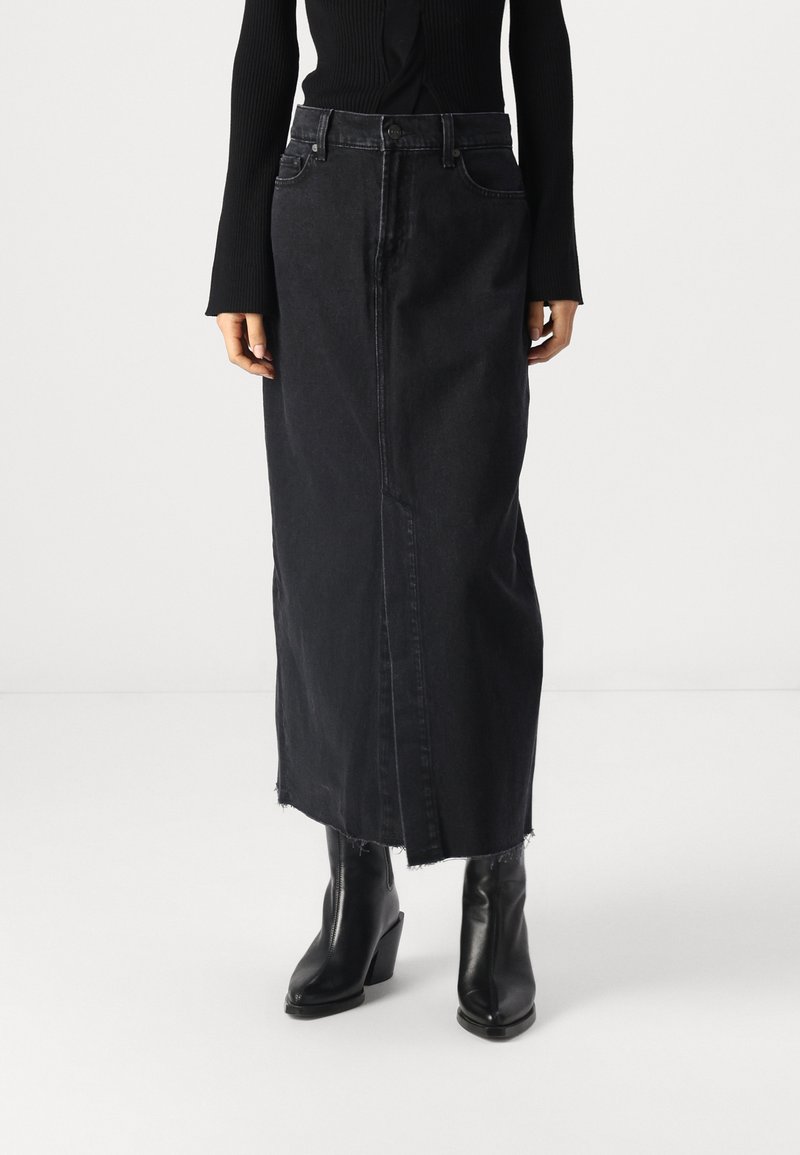 Black denim maxi skirt with a straight cut, frayed hem, and front slit. Paired with tall, chunky-heeled black boots.