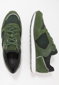 Sneakers verdi realizzati con materiali in suede e rete, caratterizzati da un motivo esagonale, dettagli bianchi e una suola in gomma grigia.