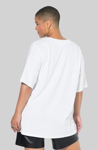 Hvid oversized t-shirt med korte ærmer, rund halsudskæring, glat tekstur og en afslappet pasform, kombineret med sorte lædershorts.