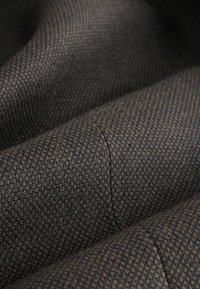 Textil mit einer strukturierten Oberfläche, braun und dunkelgrau gemustert, das weich und leicht grob ist und sichtbare Nähte aufweist.