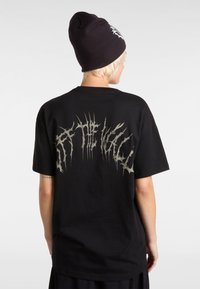 Black cotton t-shirt with a loose fit featuring a large, jagged silver graphic on the back. Paired with a black beanie.