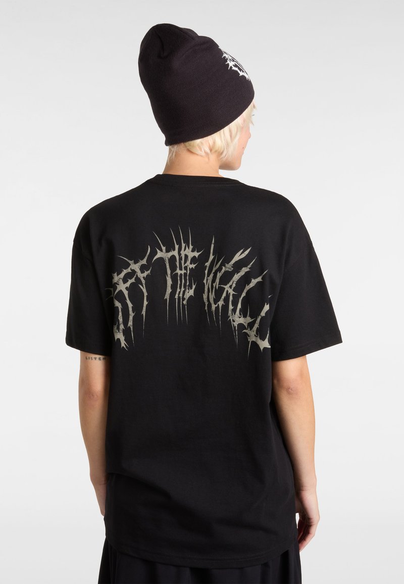 Black cotton t-shirt with a loose fit featuring a large, jagged silver graphic on the back. Paired with a black beanie.