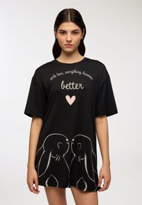 T-shirt nero oversize con conigli bianchi e argentati sagomati sull'orlo, con testo bianco sopra. Tessuto morbido, maniche corte.