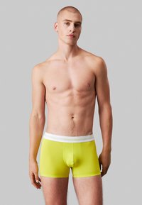 Boxer gialli luminosi realizzati in tessuto elasticizzato con una cintura elastica bianca che mostra il logo Calvin Klein; design aderente.