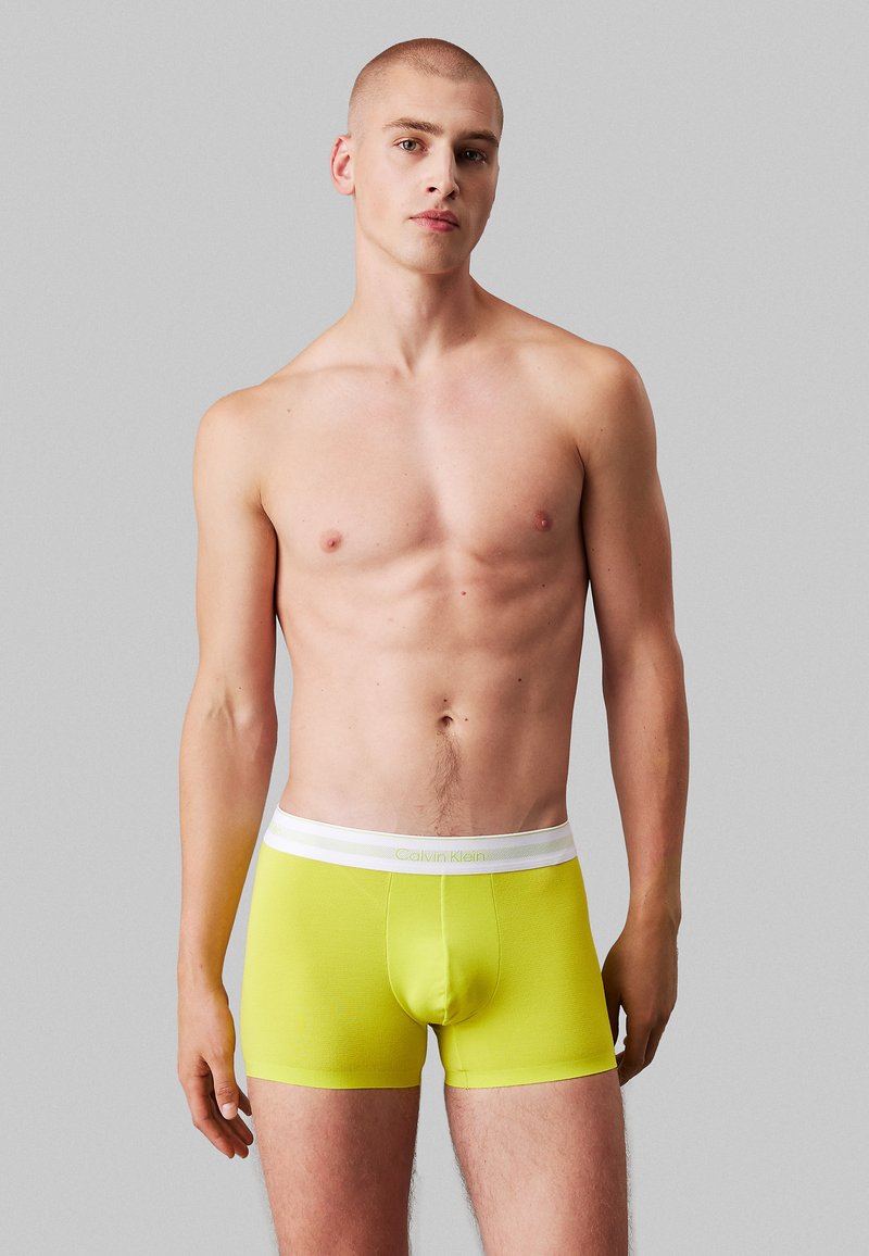 Boxer gialli luminosi realizzati in tessuto elasticizzato con una cintura elastica bianca che mostra il logo Calvin Klein; design aderente.