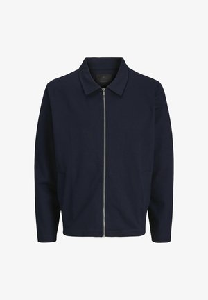 Tumes sinine tõmblukuga jakk, millel on seisev kaelus, pikad varrukad, küljetaskud ja sile kangastekstuuri. Minimalistlik disain, ilma mustrite ja aksessuaarideta.