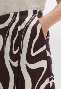 Pantaloni marroni e crema con motivo, dotati di una cintura elastica, una tasca laterale e un tessuto fluido, che presenta un design ondulato.