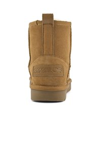 Hnědé semišové kotníkové boty s texturovaným povrchem, plochou gumovou podrážkou a štítkem s názvem značky na patě.