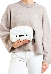 Witte, gevoerde clutch bag met een afgeronde rechthoekige vorm, voorzien van zwarte accenten, een rits en een gestructureerd smiley gezicht ontwerp.