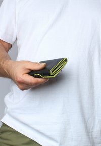 Zwarte leren portefeuille met groene accenten aan de randen. Opgevouwen ontwerp met stiksels, vastgehouden in een hand tegen een witte achtergrond.