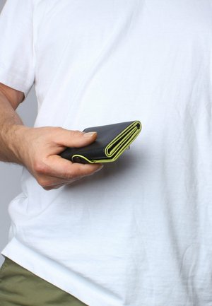 Black wallet made of leather, featuring green accents on the edges. Folded design with stitching detail, held in a hand against a white background.