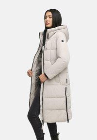 Lichtgrijze gewatteerde lange jas met capuchon, voorzien van een ritssluiting, schuine naden en zwarte afwerking. Draag het over een donkere outfit en zwarte laarzen.