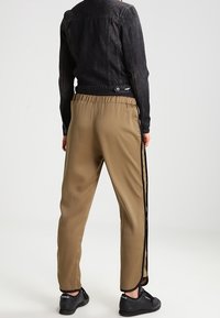 Giacca di jeans nera abbinata a pantaloni tapered beige con strisce laterali nere e vita elastica, completata da sneakers nere.