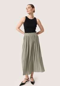 Zwarte geribbelde tanktop gecombineerd met een geplooide, knielange olijfgroene rok en zwarte slingback schoenen met spitse neus.