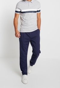 Polo gris avec des rayures horizontales bleu marine et blanches, associé à un pantalon bleu marine foncé et des baskets blanches. Tissu lisse, coupe décontractée.