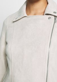 Jasnoszara zamszowa kurtka z zamkiem błyskawicznym i kołnierzem na zatrzask. Charakteryzuje się gładką fakturą i minimalnym detalem szwów.