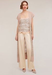 Sequined tank top under a light pink open cardigan, paired with cream wide-leg pants and embellished heels. Smooth textures and neutral colors.