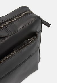 Svart läderväska med slät текстur, med metallblixtlås och stygn detaljer. Innehåller en liten extern dragkedjeficka.