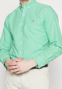Zelená a bílá kostkovaná košile na knoflíky s límečkem, s dlouhými rukávy a malým vyšitým logem na hrudi.