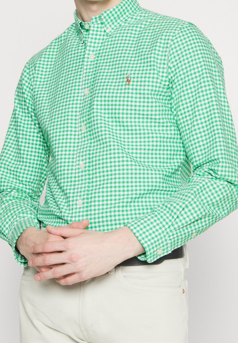 Zelená a bílá kostkovaná košile na knoflíky s límečkem, s dlouhými rukávy a malým vyšitým logem na hrudi.