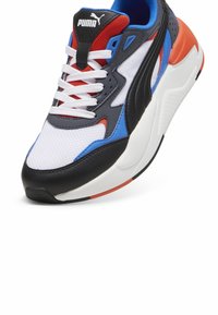 Puma tornacipők, fehér hálós felsőrésszel, fekete bőr kiegészítőkkel, piros és kék részletekkel, vastag talppal és hagyományos fűzőkkel.