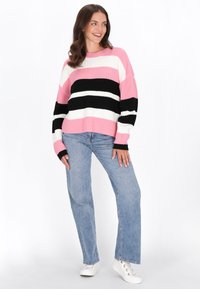 Pulover din tricot cu dungi orizontale în nuanțe de roz, negru, alb și crem. Asortat cu blugi drepti de culoare albastru deschis și teniși albi.