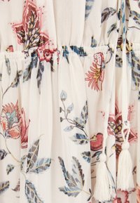 Tejido ligero con estampado floral en azul, rosa y marrón, cintura elástica fruncida y detalle de lazo con borlas blancas.