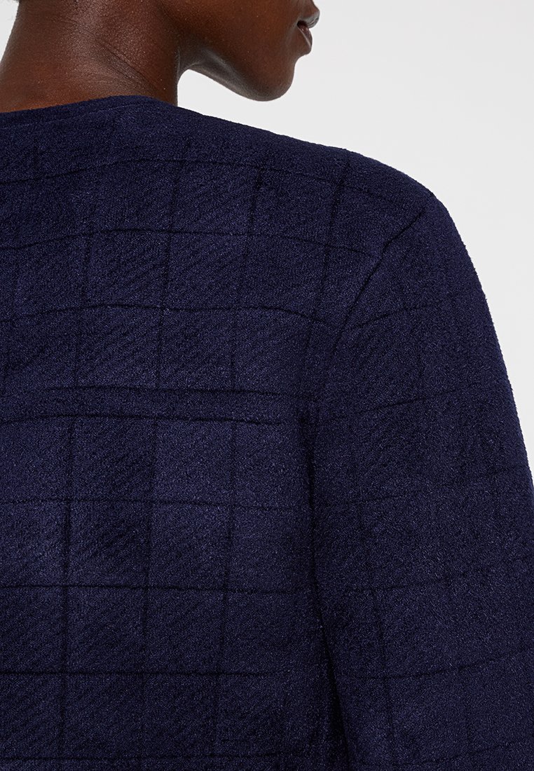 Granatowa, teksturowana odzież z wzorem siatki. Tkanina wydaje się pluszowa, ma miękką, dotykową powierzchnię i zdefiniowaną sylwetkę.